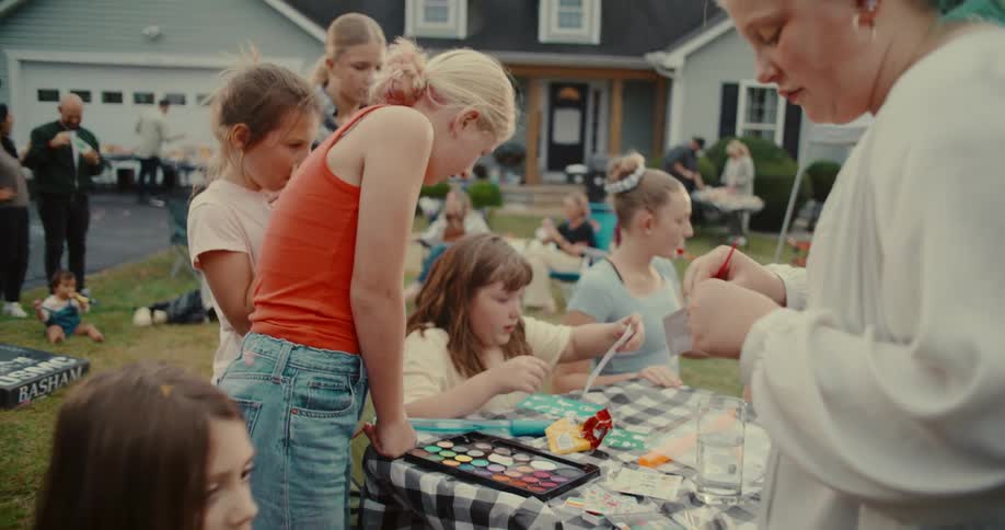 Kids gather around an arts and crafts table for face painting at a lively neighborhood block party