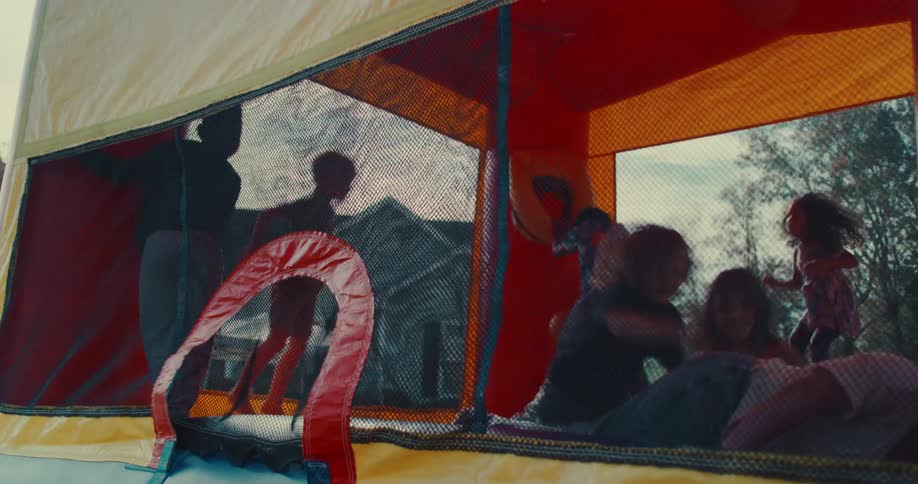 Slow motion side view of kids jumping inside a red and yellow bounce house at a party