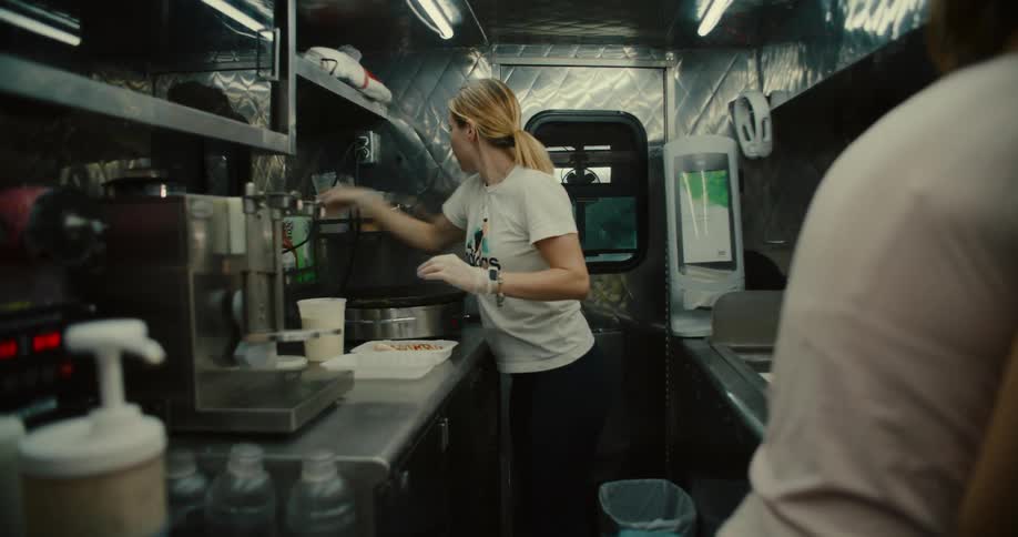 A woman carefully prepares an order in the stainless steel kitchen of a busy food truck