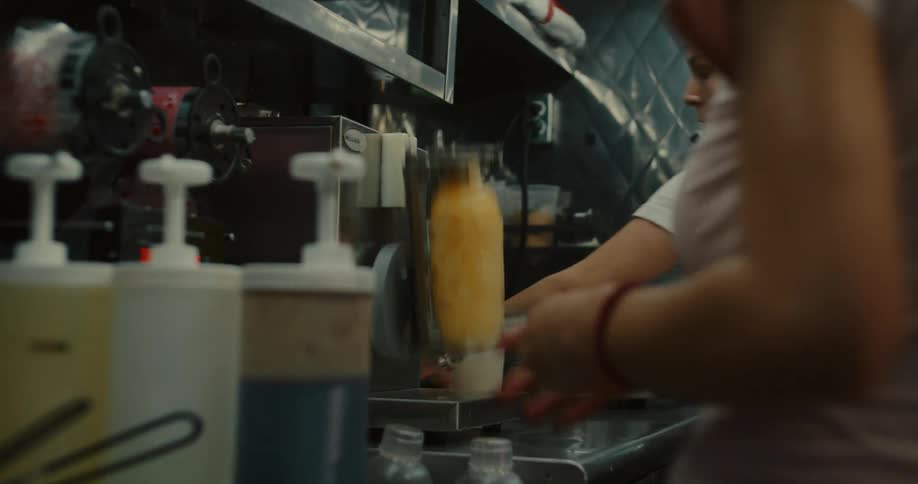 A food truck employee makes a blended drink with a shaker machine while working in the kitchen