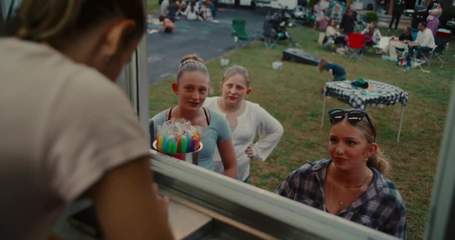 A group of young women order refreshing drinks from a food truck window at a lively outdoor party