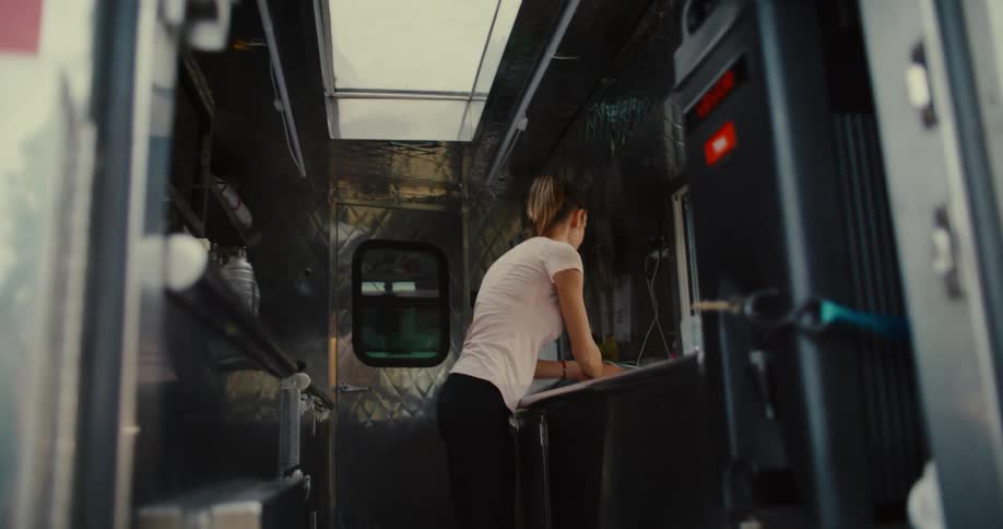 A female food truck worker diligently prepares her stainless steel mobile kitchen for a day of service