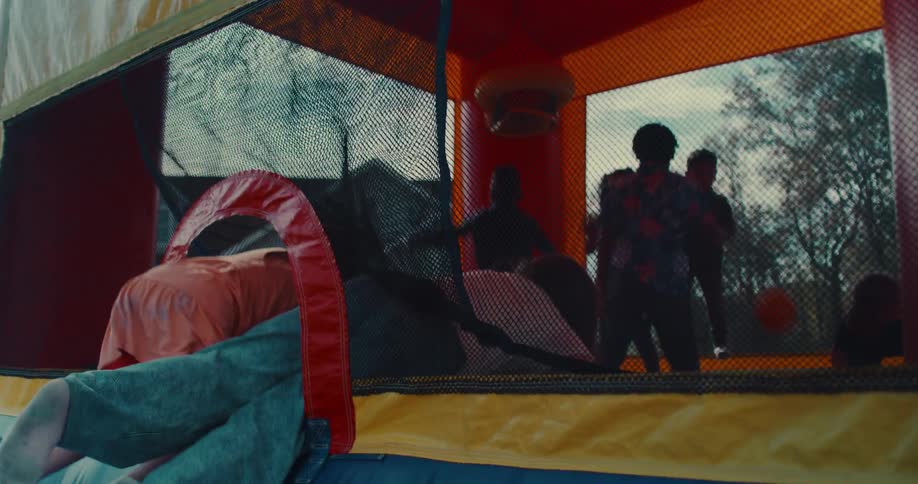Kids and adults crawl into a colorful bouncy castle to jump and play together at a backyard party in slow motion