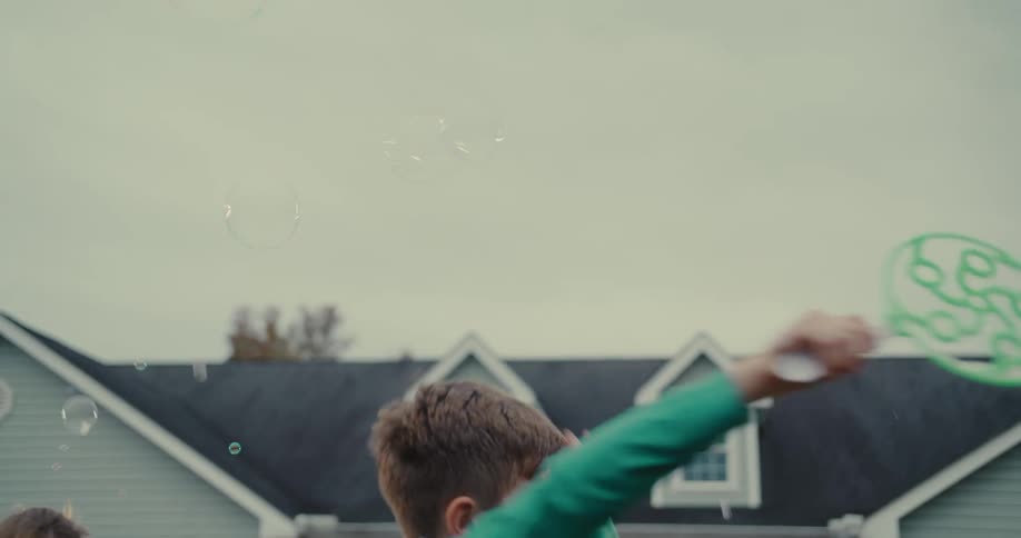 Joyful children play with giant soap bubbles in slow motion during a lively neighborhood party in the front yard