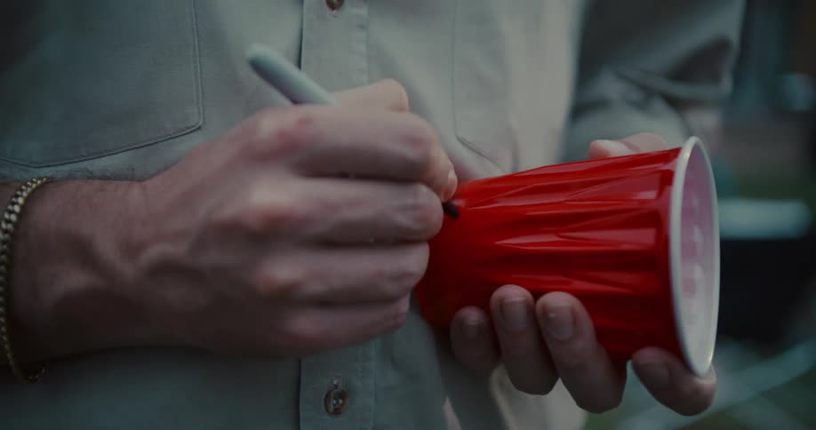 A man writes his name on a red plastic cup with a marker at an outdoor party
