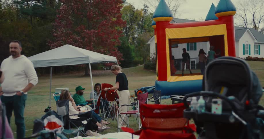 Families gather for an outdoor party as children jump in a bouncy castle in the backyard on a cloudy day