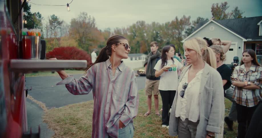 Two women at the front of the line order from a red food truck during a casual outdoor party