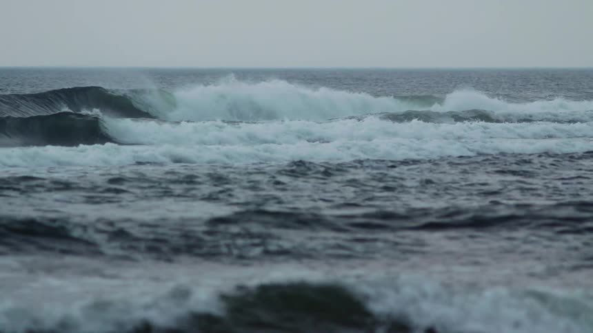 Surfers floating as large waves roll and crash in the ocean
