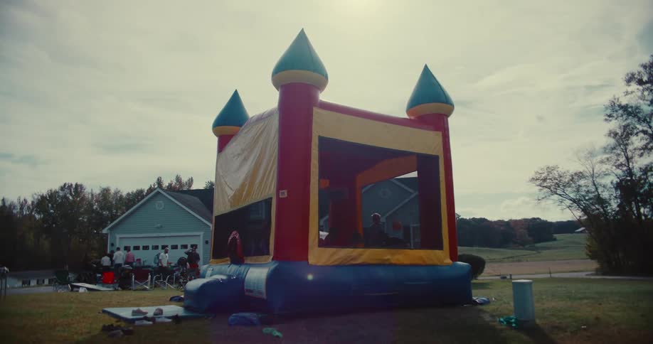 Kids joyfully jump in a colorful bounce house in slow motion during a sunny backyard party