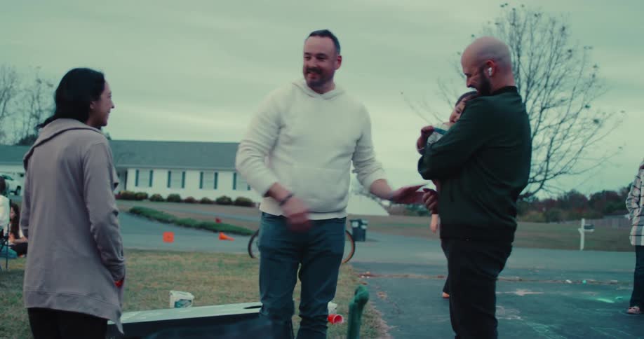 Friends and family greet each other warmly with hugs and handshakes at a casual outdoor gathering in the neighborhood