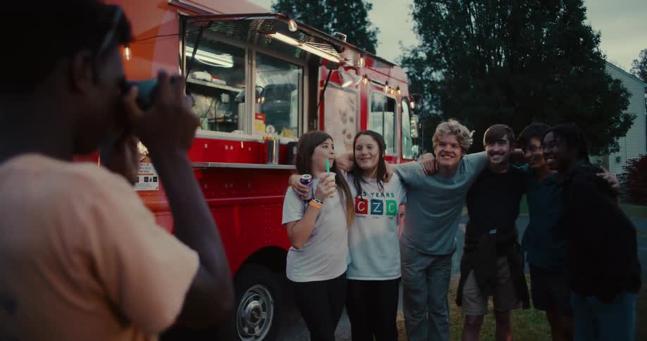 A diverse group of happy teenage friends poses for a photo in front of a red food truck at dusk