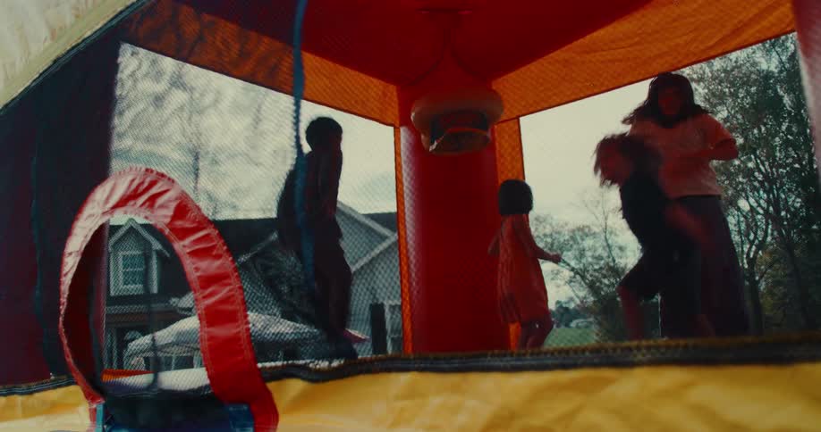 Slow motion footage captures a group of children having fun as they jump and play inside a colorful bounce house at an outdoor party