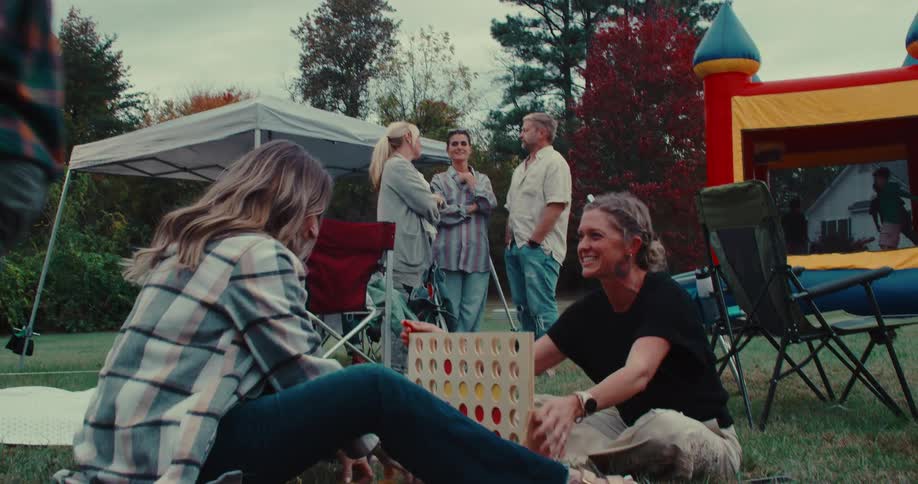 Family and friends enjoy an outdoor party, playing lawn games and socializing in a backyard with a bouncy castle