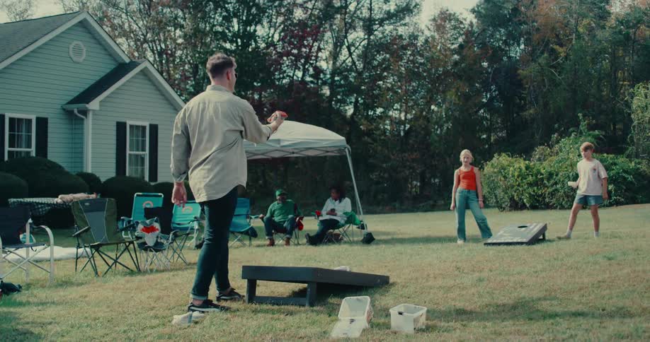 Friends and family play cornhole in the backyard during a sunny outdoor gathering in slow motion