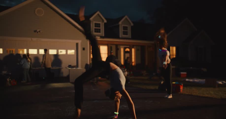 Two young women with glow sticks perform impressive gymnastics and dance moves in slow motion in a driveway at night