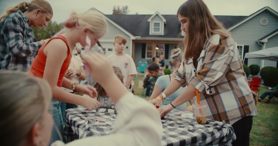 Teens and children gather around a checkered table to paint and get creative at a fun outdoor community event