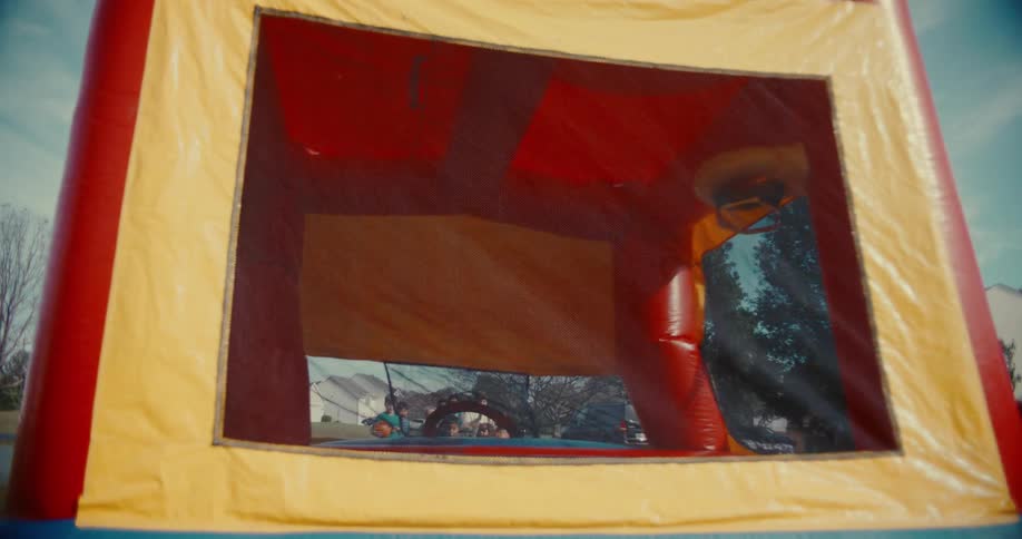 An outdoor bouncy castle is inflated with a blower before children begin to joyfully jump and play inside