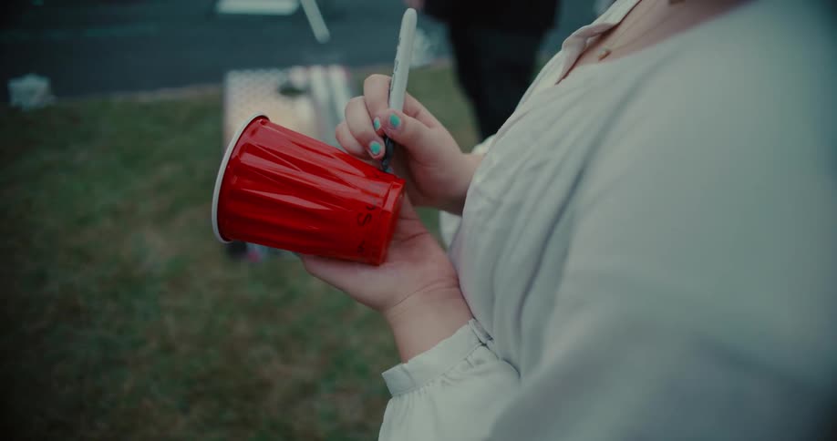 A woman's hands with painted nails are seen writing on a red solo cup with a marker at an outdoor party