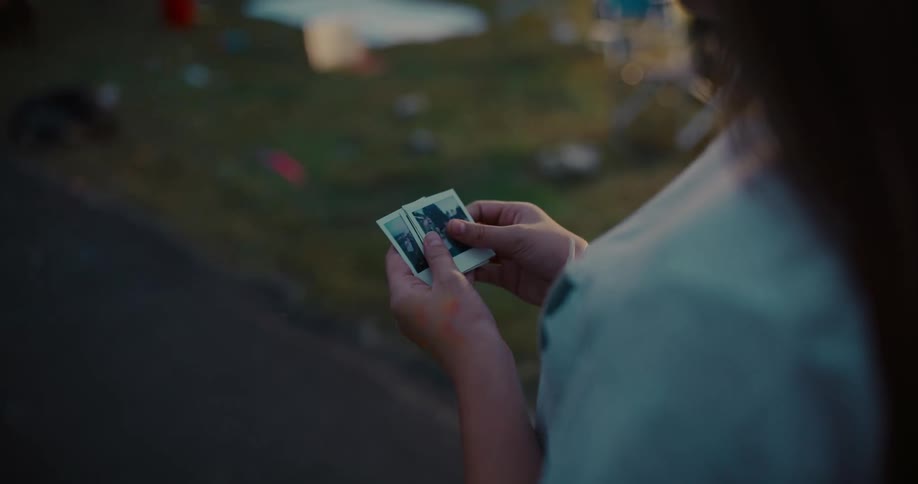 An over-the-shoulder shot captures a person holding and fanning out a small stack of instant photos, reminiscing over memories