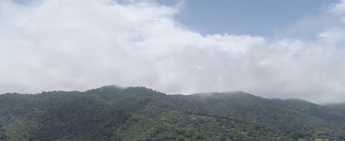 A tranquil landscape view of dense green mountains with mist and clouds rolling over the peaks
