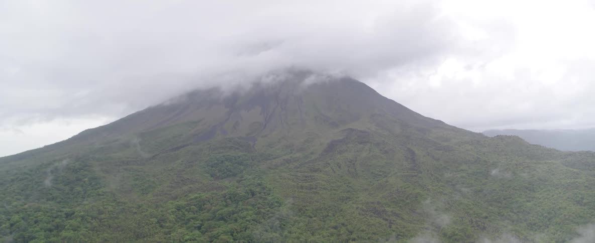 An expansive view of a verdant volcano, its summit disappearing into a thick layer of rolling clouds and mist