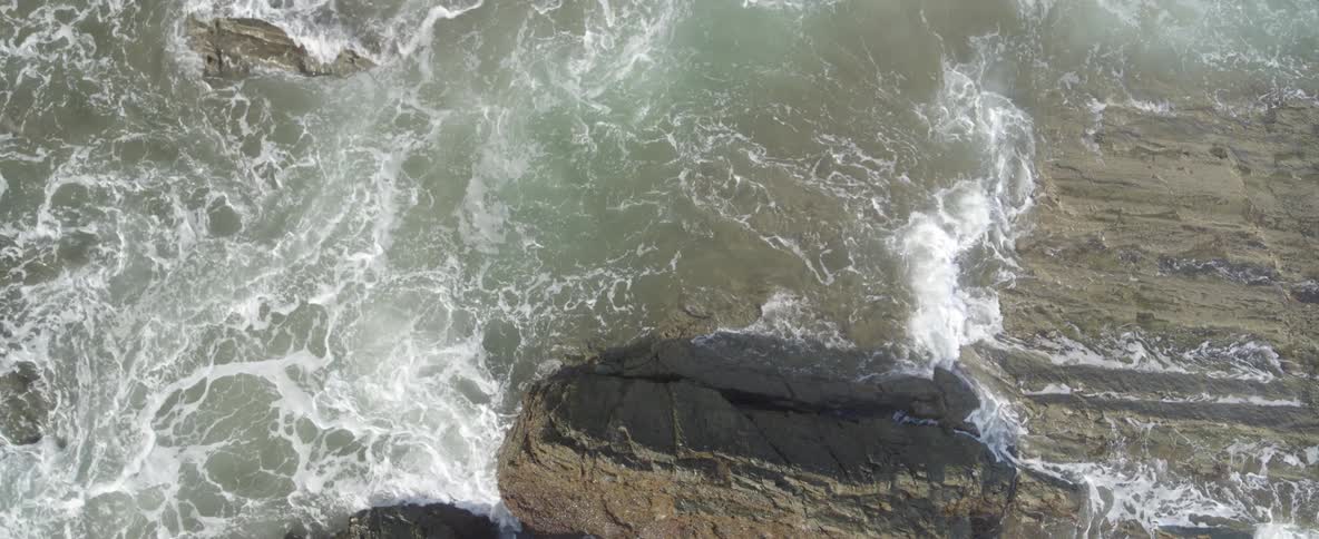 A top-down view of powerful ocean waves crashing against a rocky shoreline
