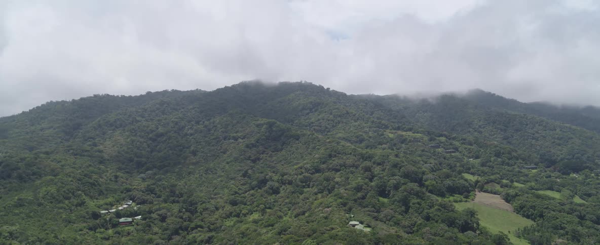 An ascending aerial shot reveals a vast tropical jungle covering a mountainous landscape with low-hanging clouds and fog