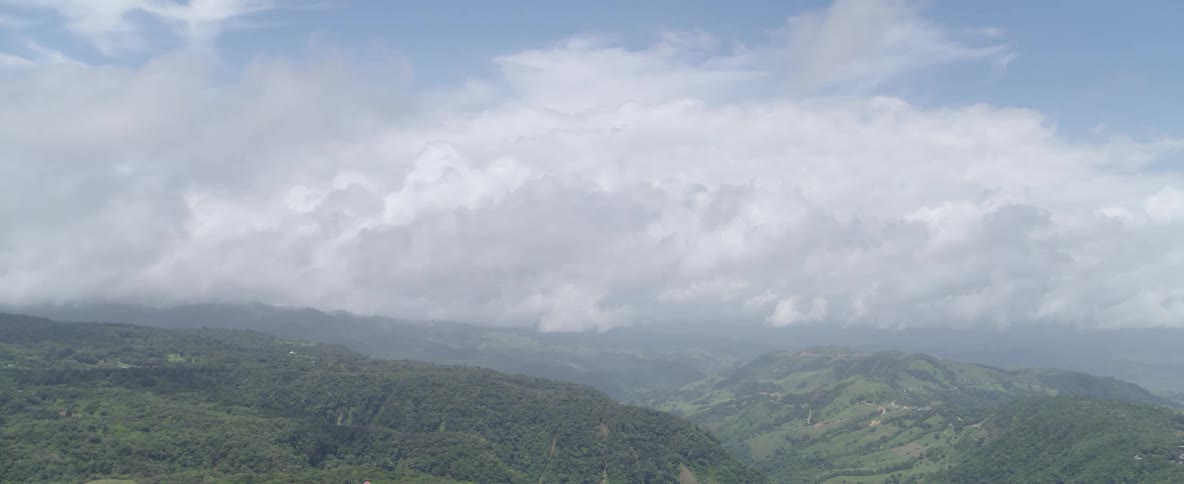 Expansive aerial view of a small town nestled in a lush, green mountain valley under a blanket of thick clouds