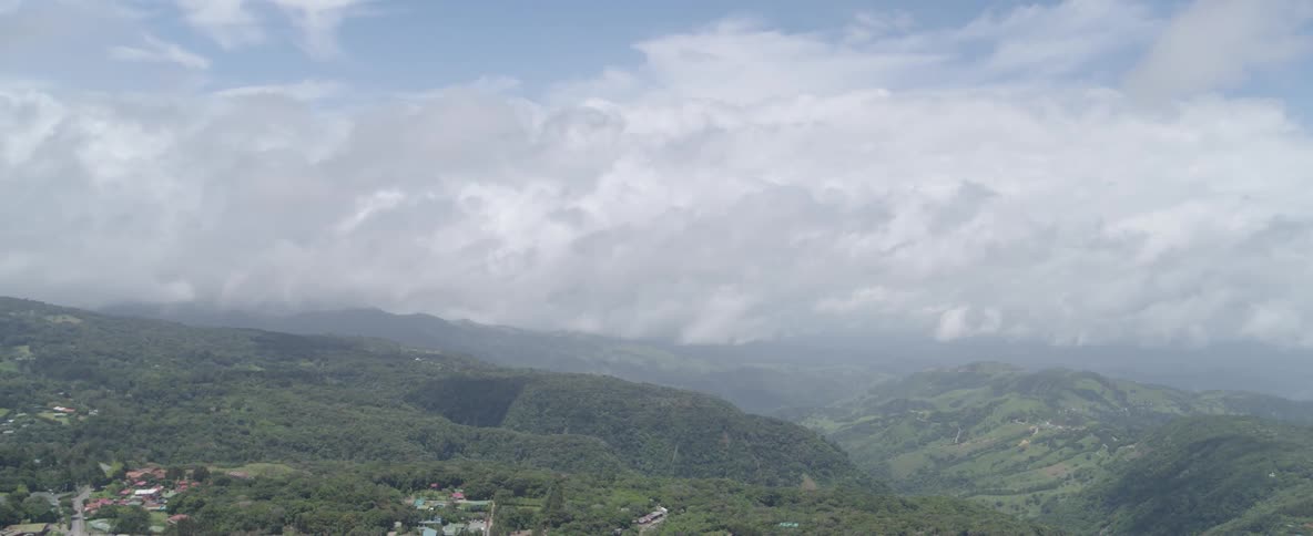 A peaceful, wide shot shows a vast mountain landscape covered in lush forests with clouds hanging low over the peaks