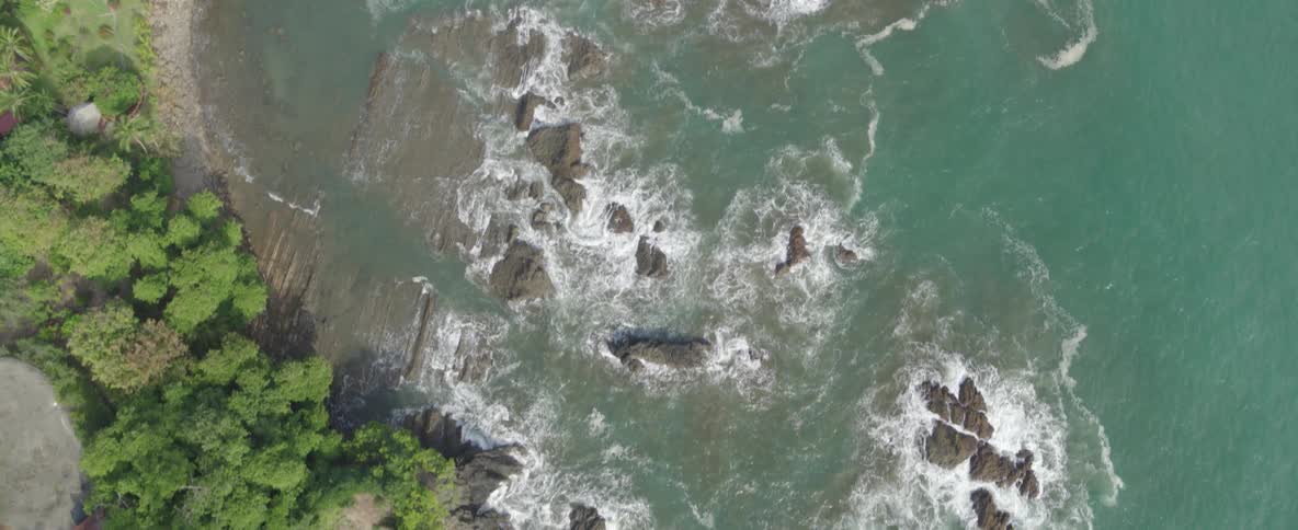 Top-down drone footage pulls away from a small, verdant island to reveal the rugged, tropical coastline where the jungle meets the sea