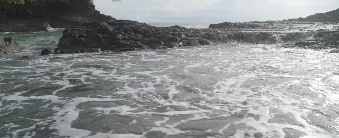 Calm ocean water flows over a rugged, rocky coast in a serene slow motion scene