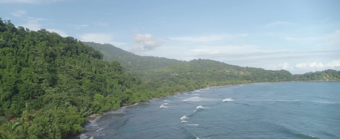 A slowly revealing aerial view of a stunning tropical coastline with a verdant jungle and calm ocean waves
