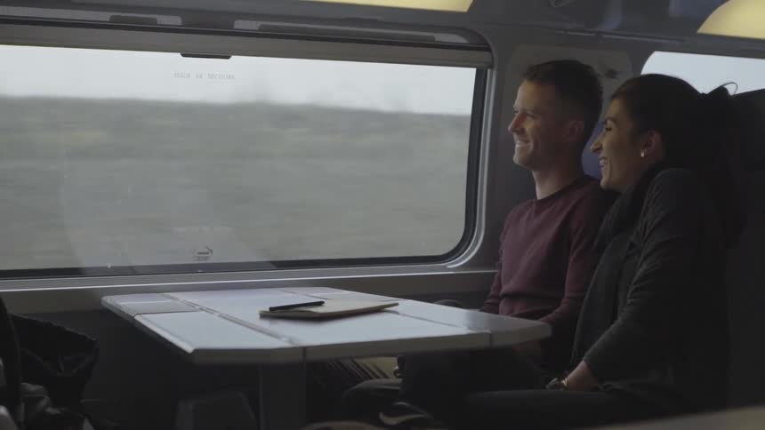 A man and woman smile while sitting in a train car