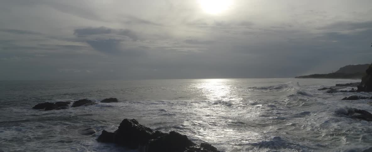 An aerial camera rises slowly over powerful ocean waves crashing against rocks in slow motion