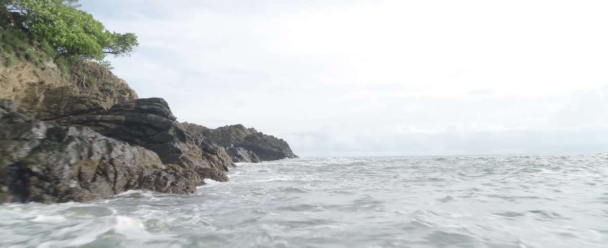 A smooth forward tracking shot glides over a rocky coastline and out into the vast, open ocean on an overcast day
