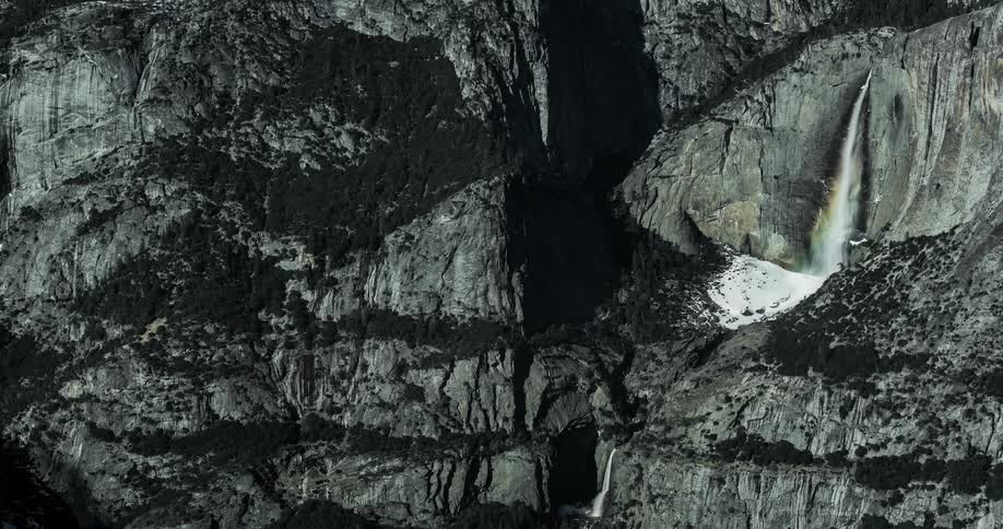 Clouds cast shadows on a rocky cliffside and waterfall