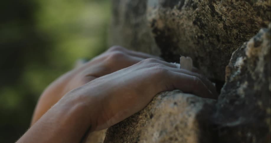 A person uses their hands to reach up and grab hold of a stone in preparation for climbing