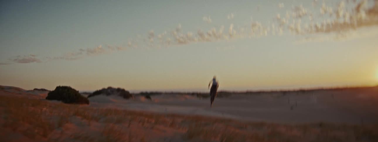A motocross rider soars through the air in slow motion, performing a big jump over sandy dunes during a beautiful sunset