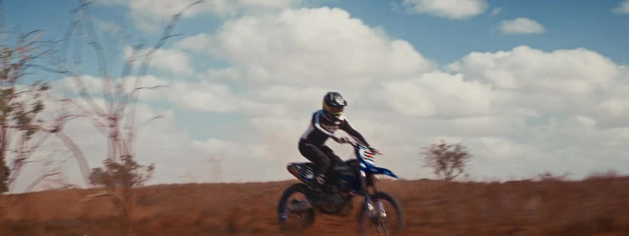 A motocross rider speeds around a corner on a dusty dirt track in a cinematic slow-motion shot