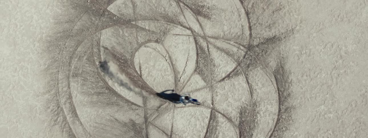 A top-down aerial shot shows a motocross rider creating abstract patterns with tire tracks in the dirt
