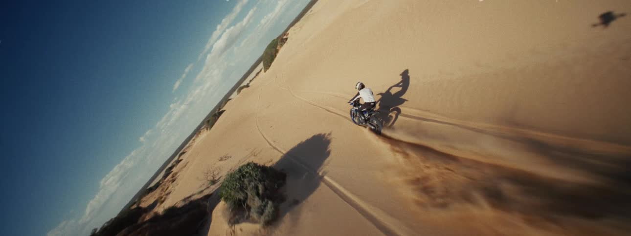 A thrilling FPV drone shot follows a motorcyclist as they race across vast, sun-drenched sand dunes