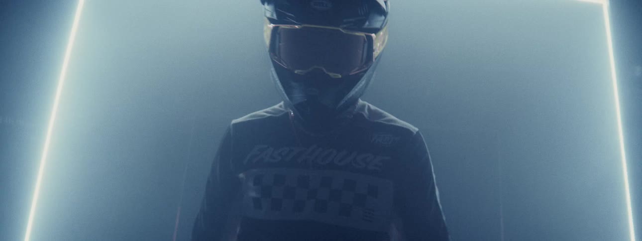 A motocross rider in full gear emerges from a dark, hazy corridor illuminated by flashing neon and strobe lights