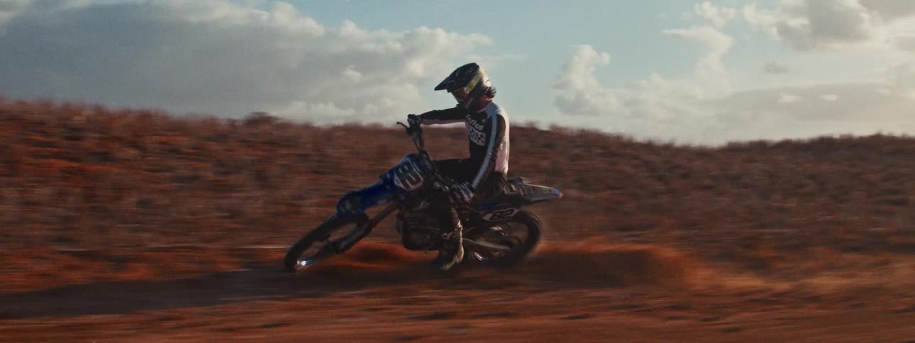 Cinematic slow motion shot of a motocross rider speeding down a dirt track at sunset