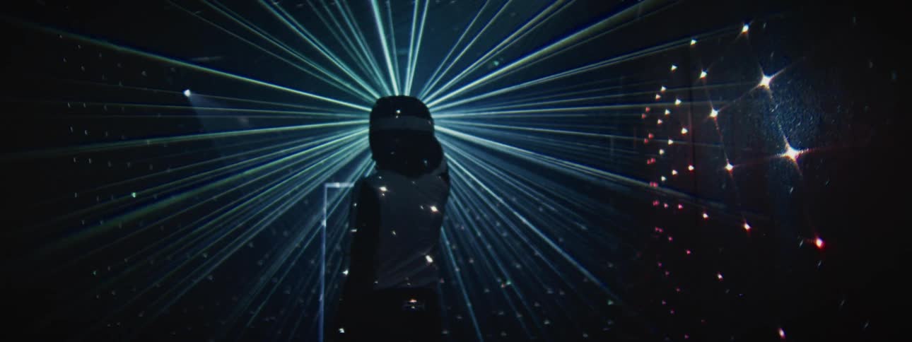 A person wearing a motocross helmet and reflective suit stands in the middle of a stunning laser light show in a dark room