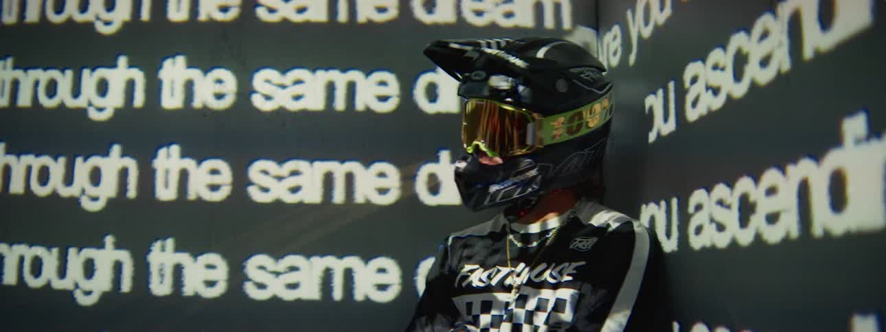 An artistic shot shows a person in a motocross helmet with abstract, glitchy text projected across their body