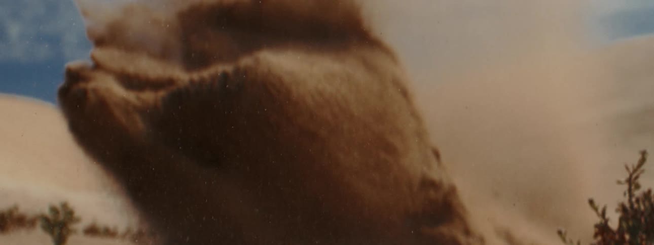 A cloud of sand explodes upward in an extreme slow-motion close-up shot in the desert