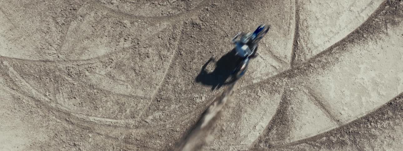 Aerial top-down slow-motion view of a motocross rider speeding along a dusty dirt track
