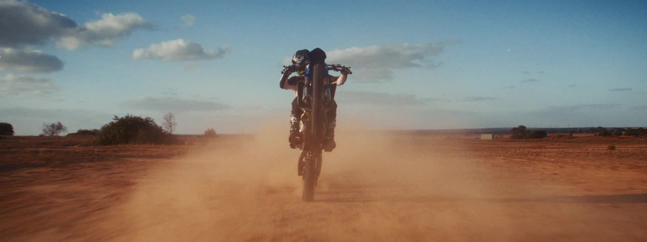 A skilled motocross rider in full gear performs a wheelie while speeding down a dusty desert track in slow motion