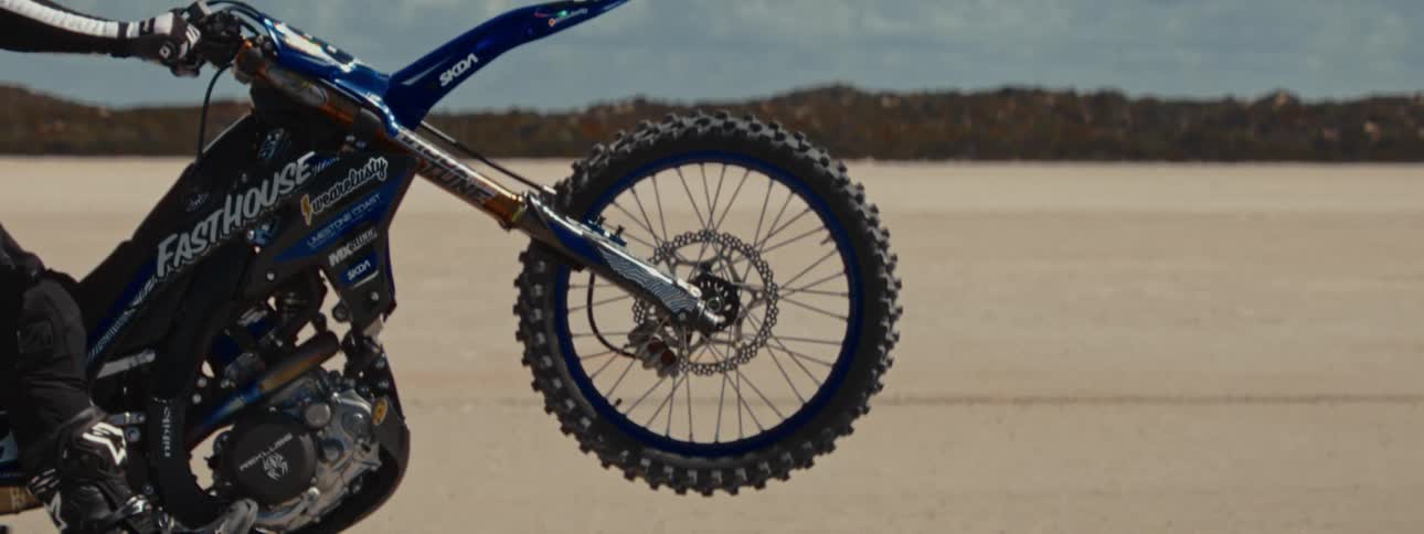 A close-up of a motocross bike's rear wheel spinning in a vast desert landscape