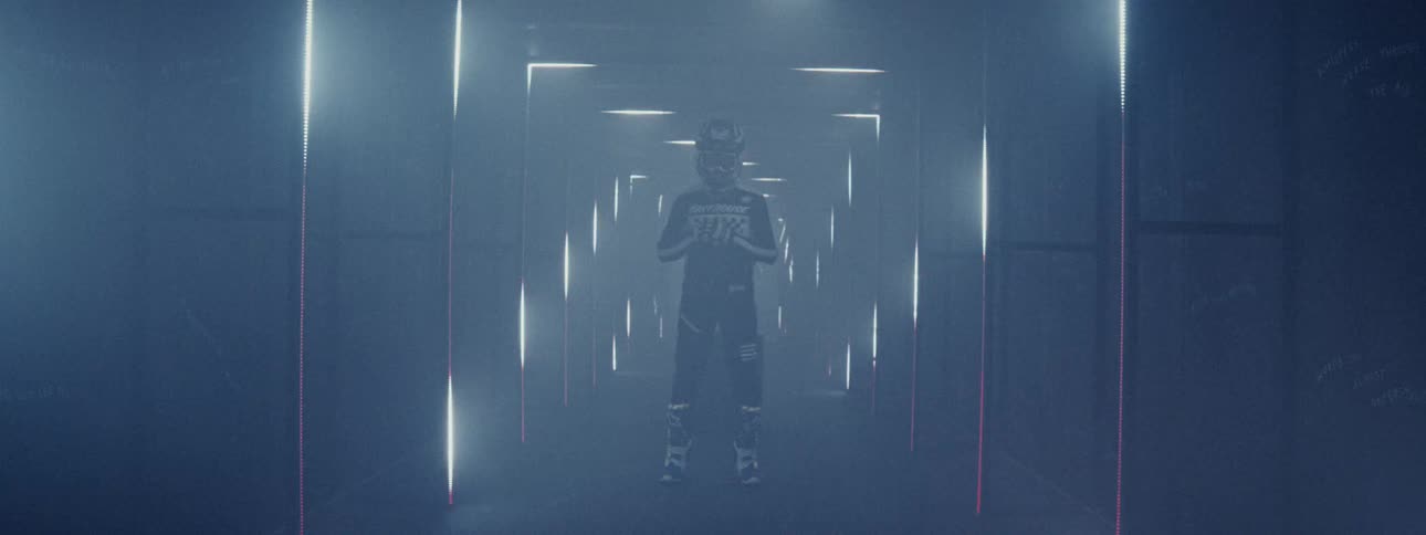 A motocross racer in full gear stands in a smoky, futuristic corridor with shifting red and white lights